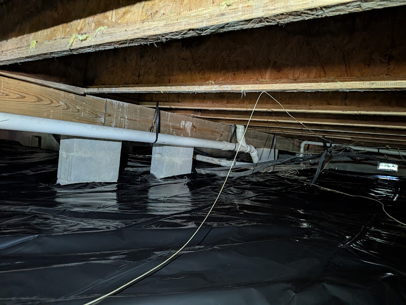 Vapor barrier sealed around block piers with plumbing lines running overhead